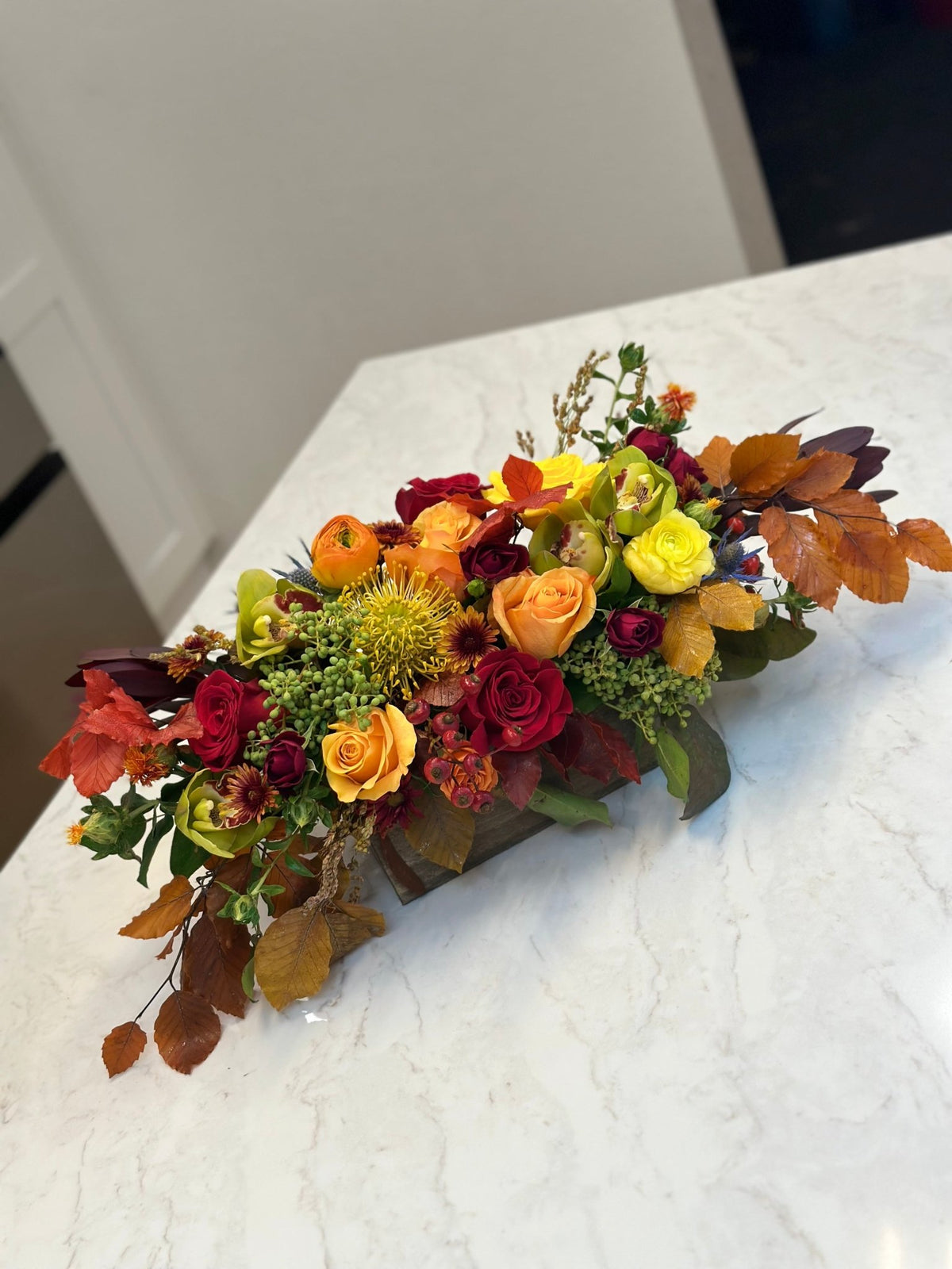 Angled view of a low fall centerpiece with roses, green orchids and copper beech leaves