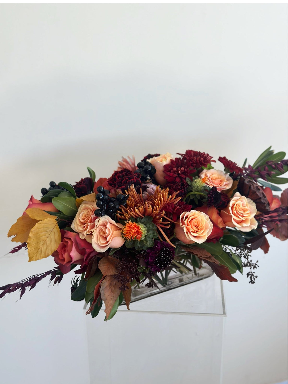 Side view of a low autumn centerpiece with peach roses, burgundy blooms and golden foliage