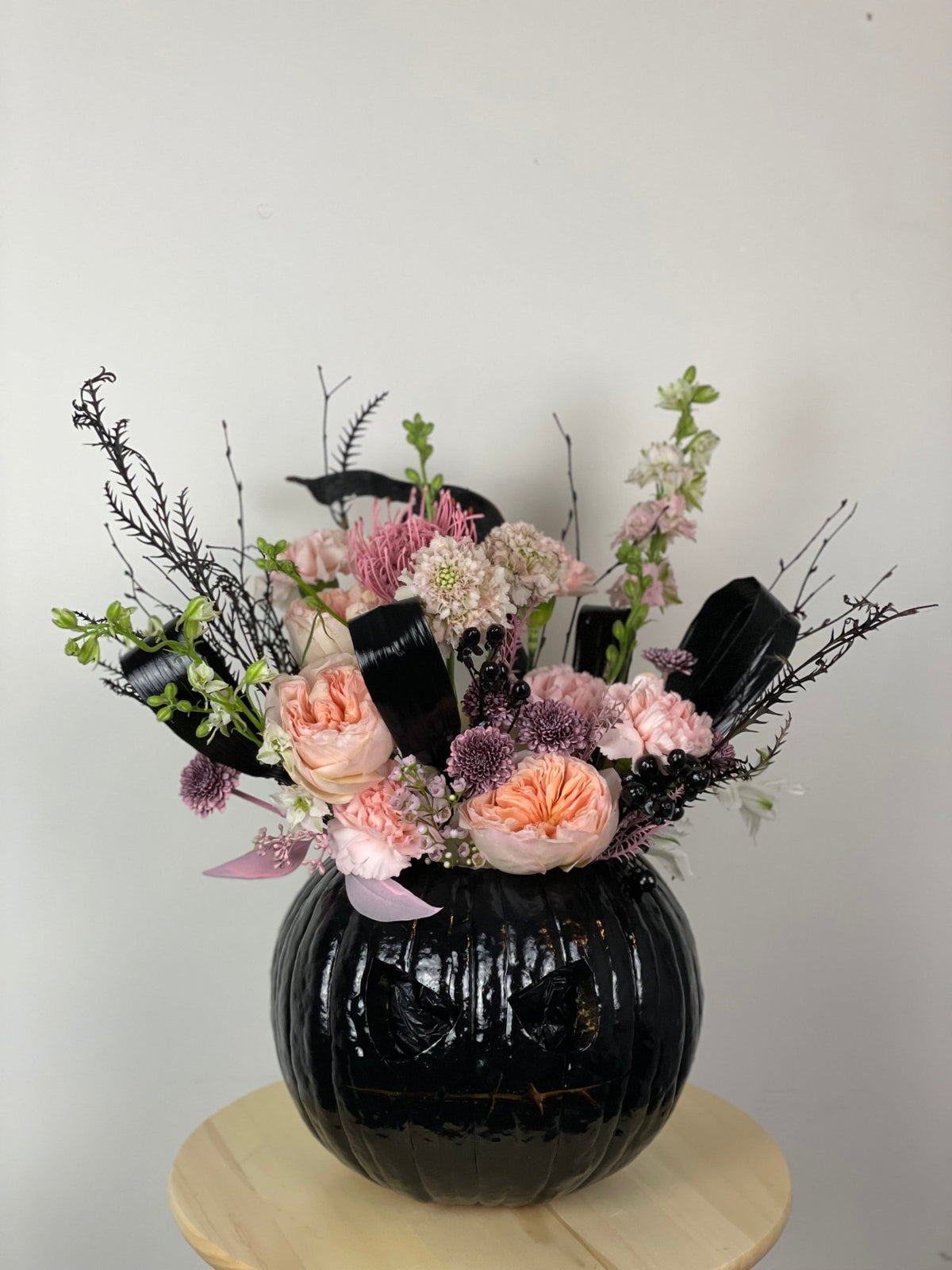 Jack-o'-Lantern arrangement of peach garden roses, carnations, scabiosa and black accents in a carved glossy black pumpkin