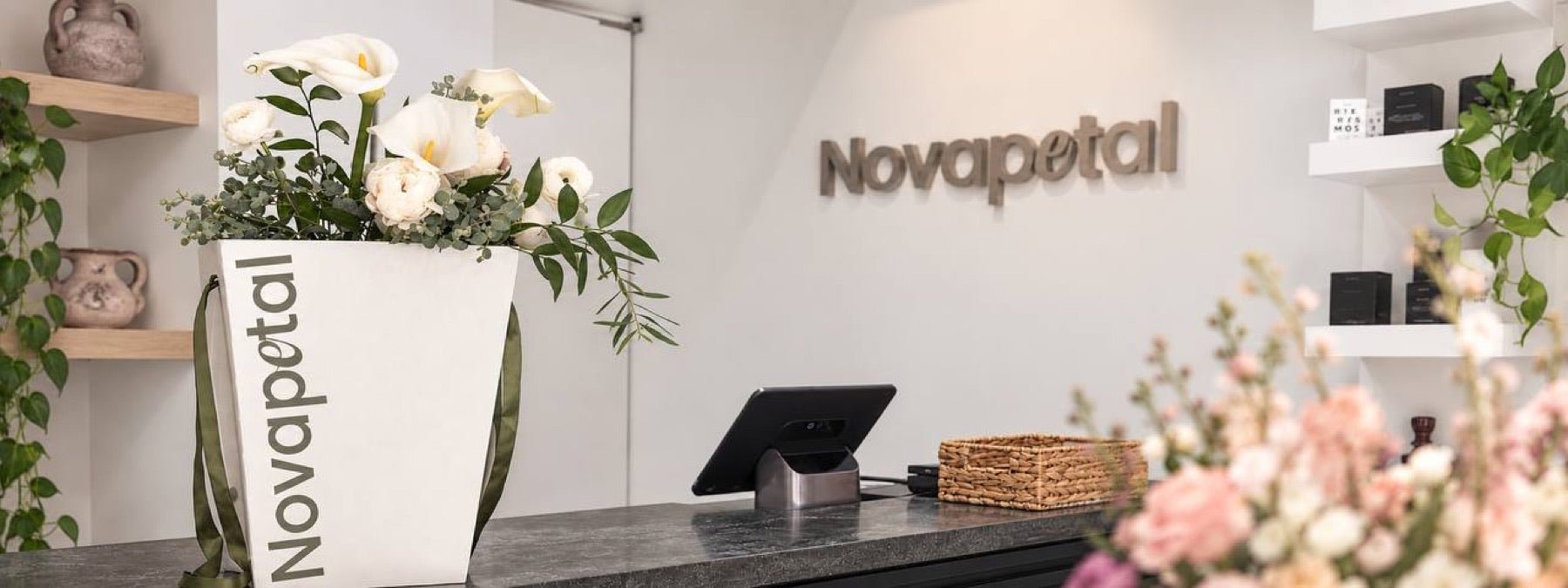 The Novapetal counter on the Upper East Side with the studio wordmark on the wall and a branded bag of white calla lilies and ranunculus