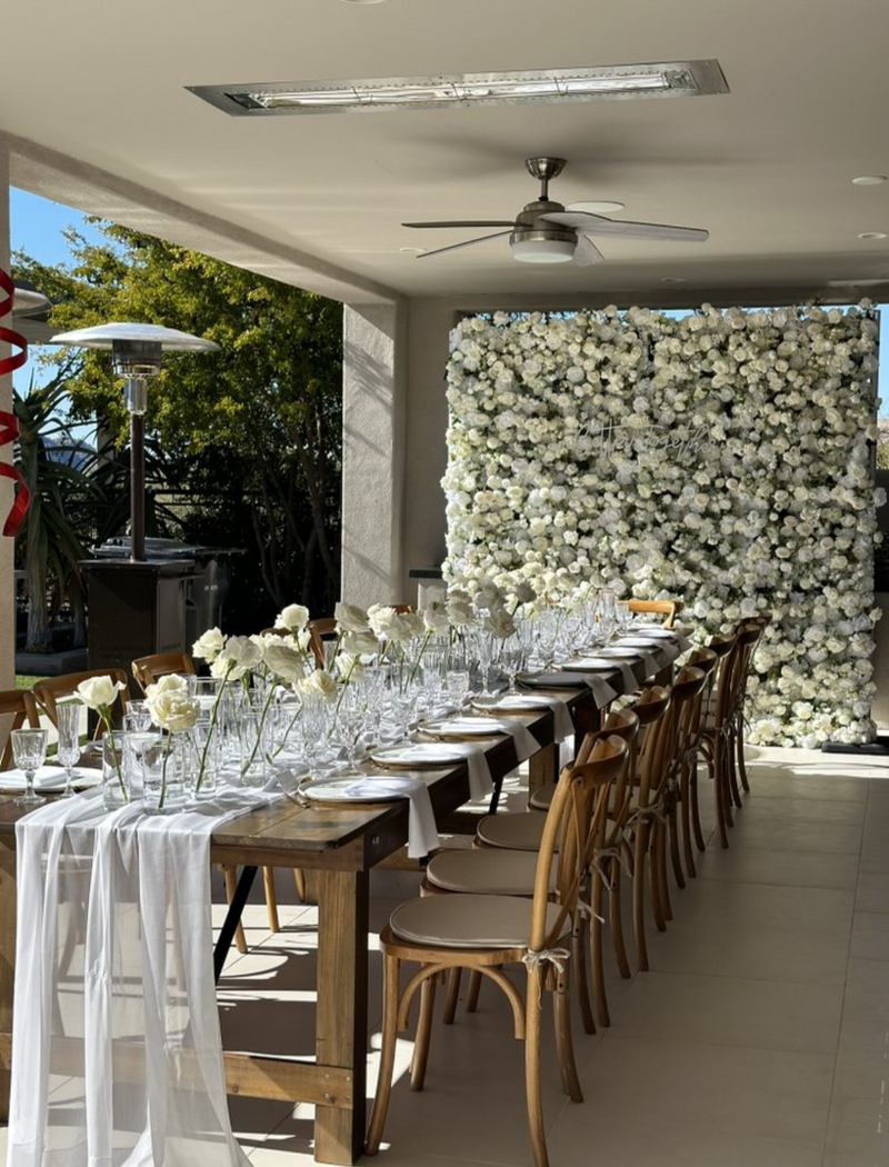 Long reception table set in white in front of a white flower wall