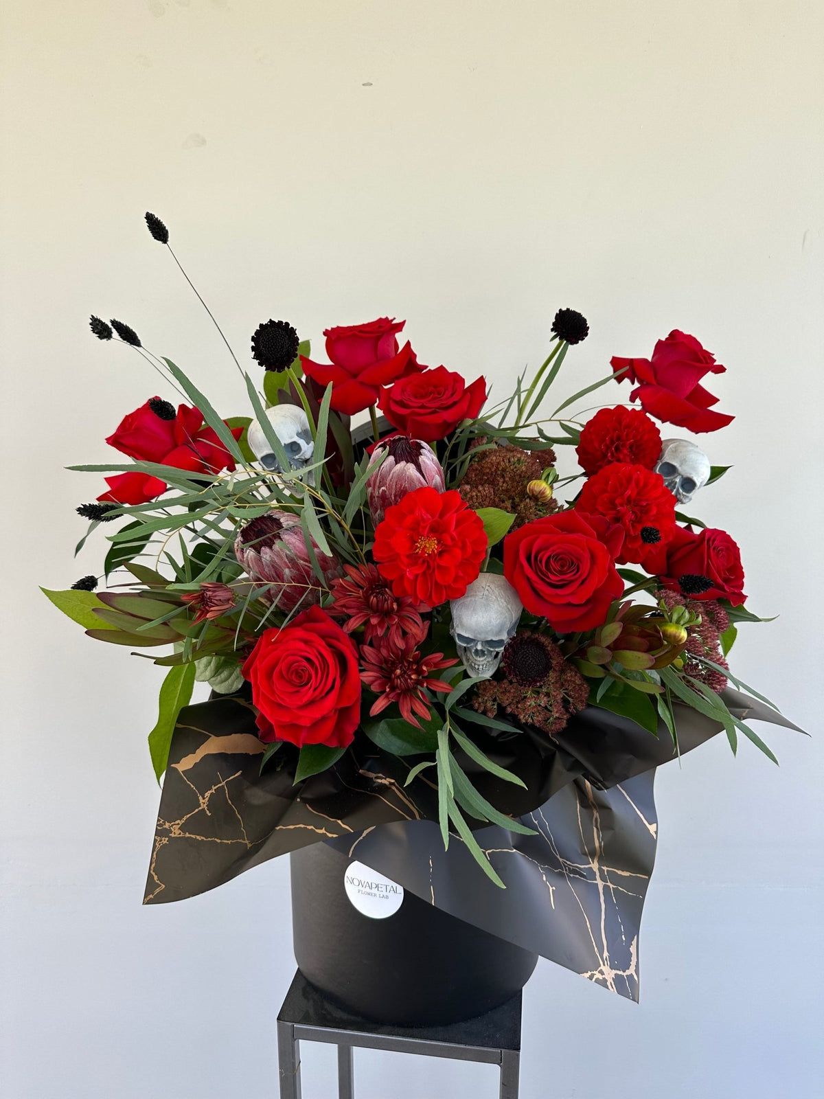 Halloween Rose Box of red roses, dahlias, proteas and black scabiosa with small skulls in a black box with gold marbled wrap