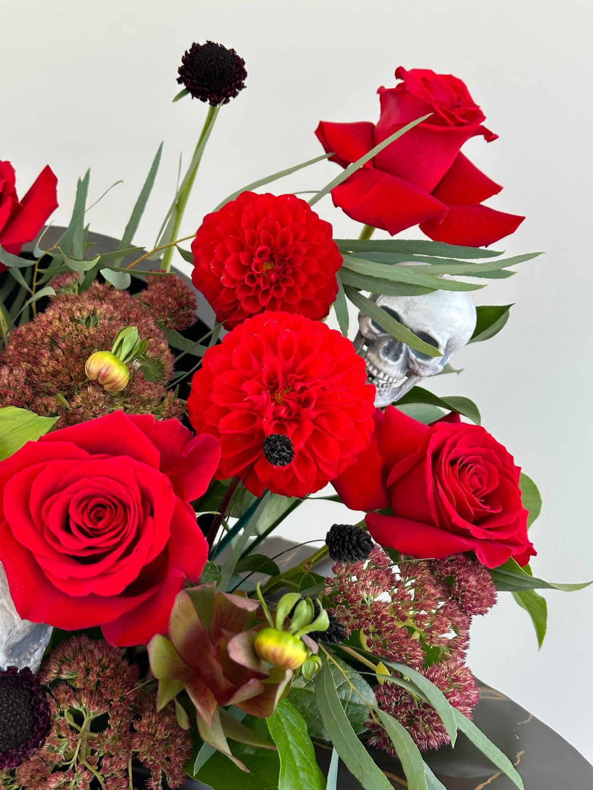 Close up of red roses, red dahlias, sedum and a small skull in the Halloween Rose Box