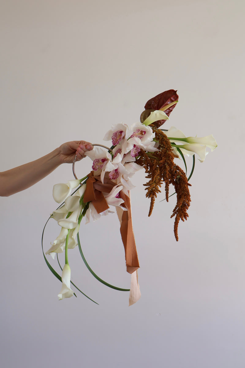 Copper and blush calla lily bridal bouquet held against a plain wall
