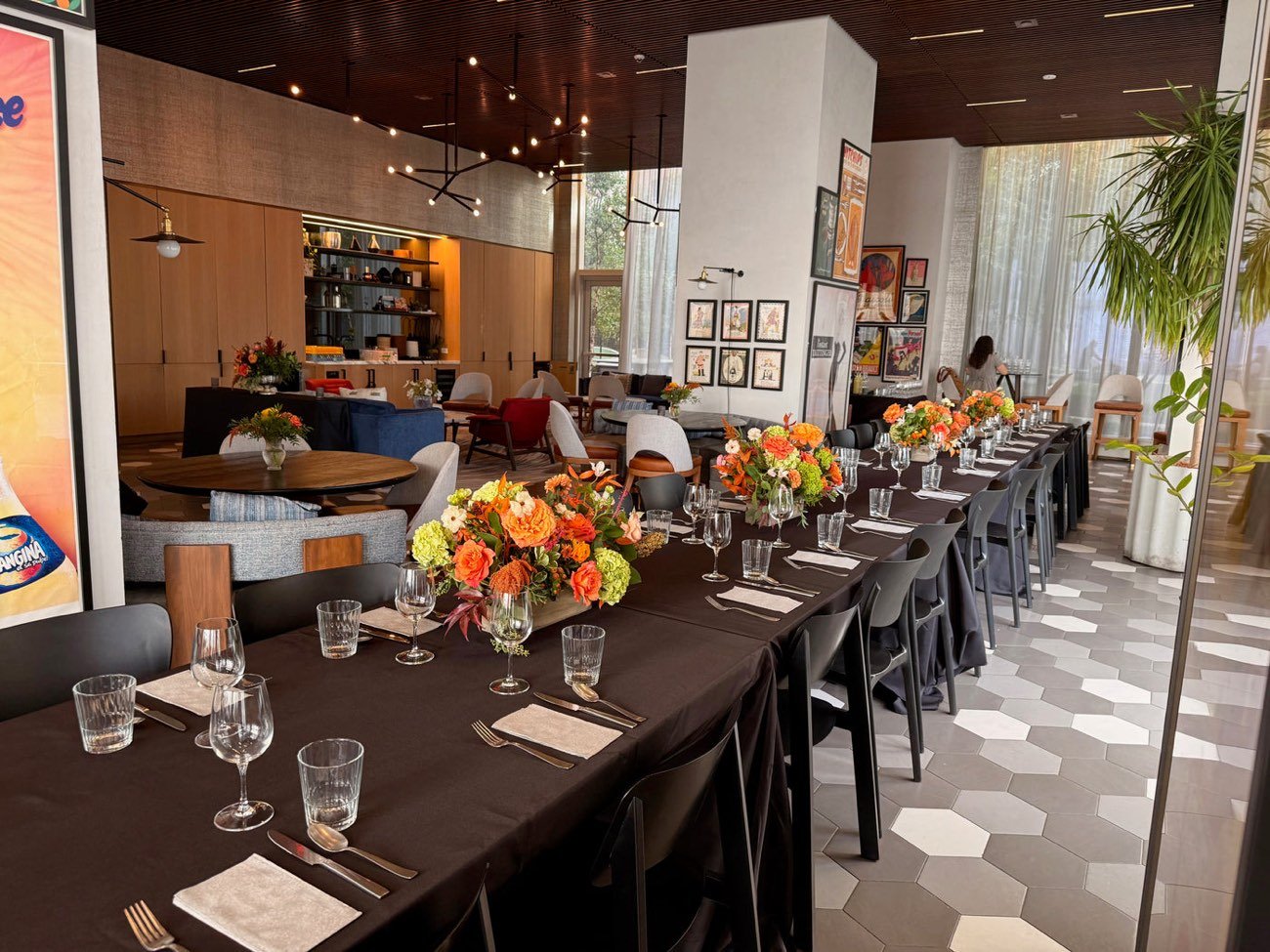 Long restaurant table set for a corporate dinner in New York with orange rose and hydrangea centerpieces down the centre