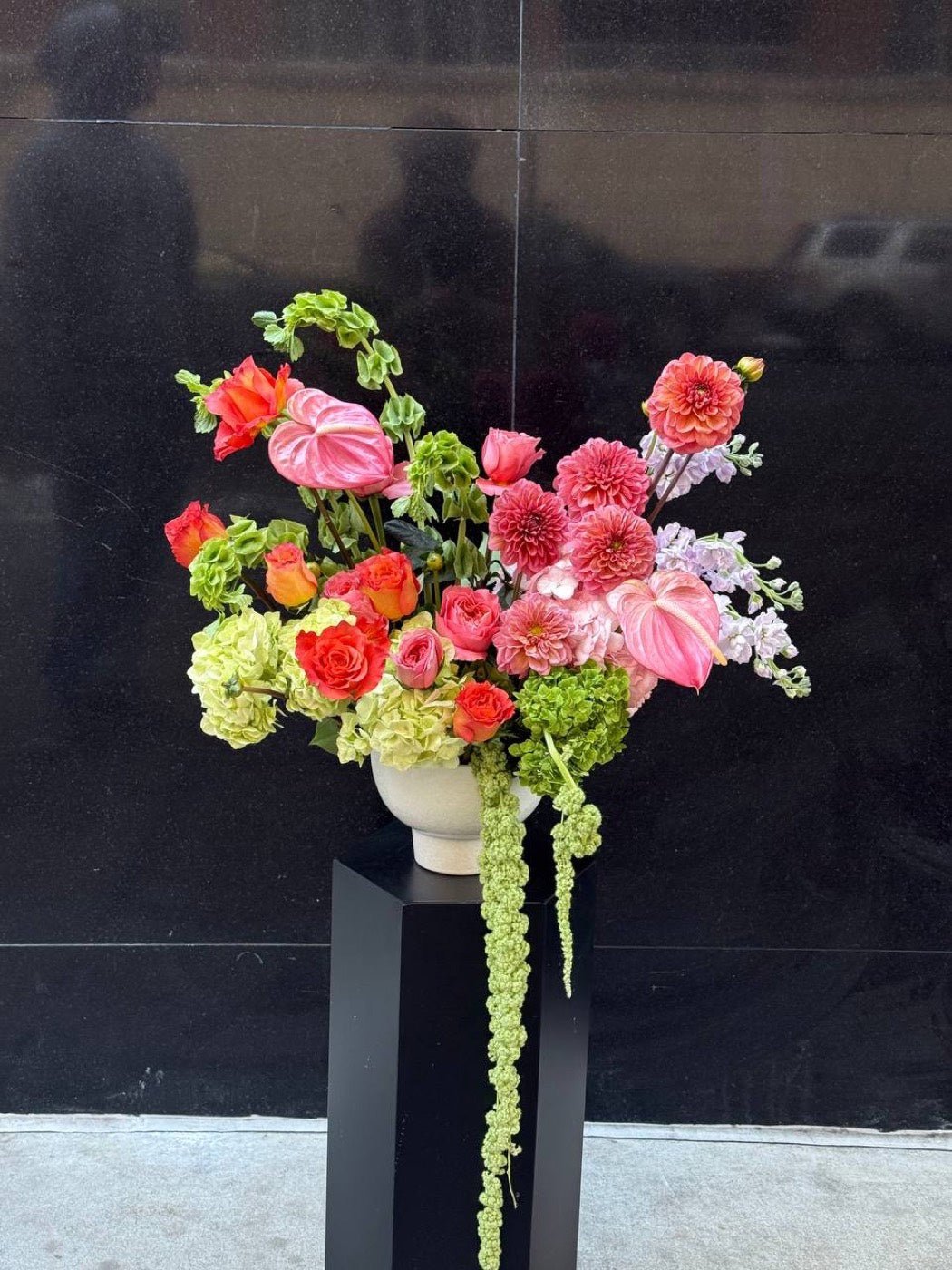 Coral rose, dahlia and anthurium arrangement on a black pedestal