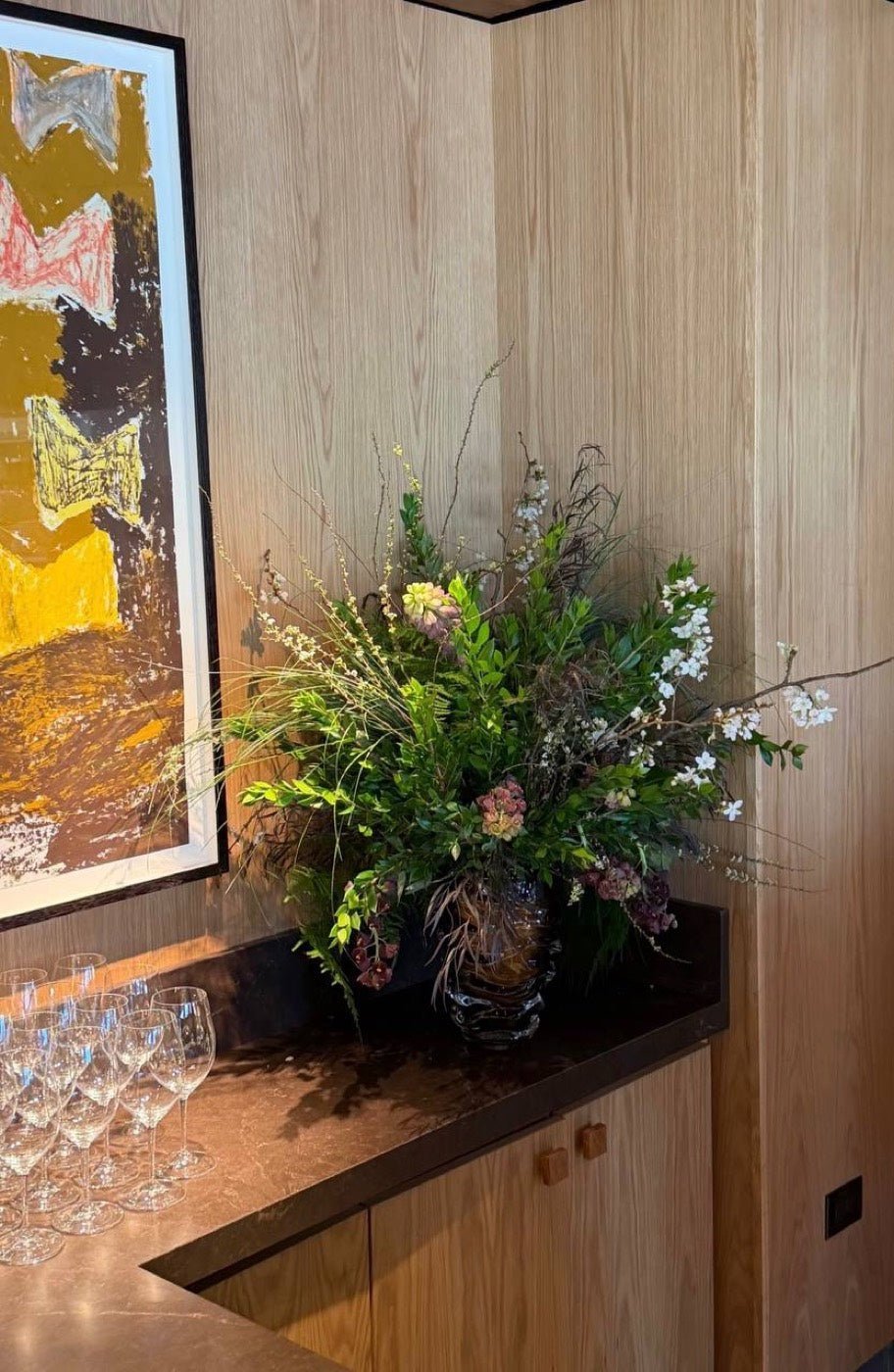 Garden-style arrangement with blossom branches and trailing greenery in an interior