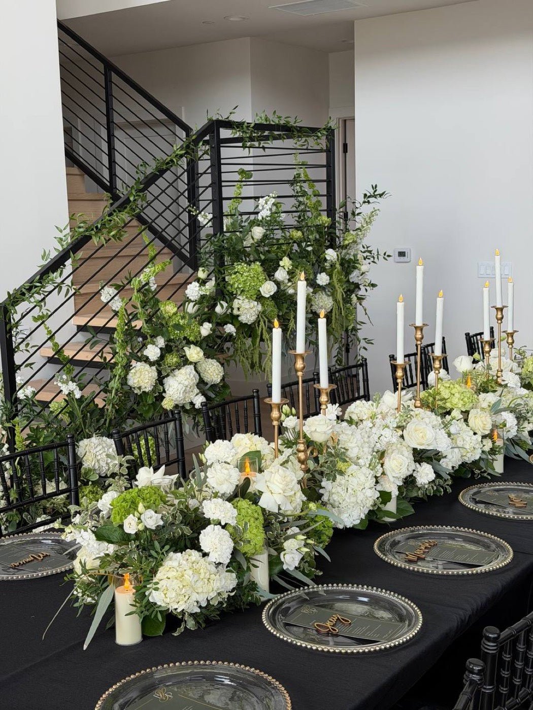 Long banquet table with black linen, silver chargers, a white hydrangea and rose runner and gold candlesticks at a corporate dinner in New York