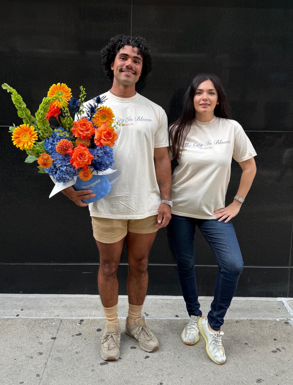 Olga and Anthony Sheppard outside the Novapetal studio in New York, in Novapetal t-shirts, holding an orange and blue arrangement in a branded Novapetal vase