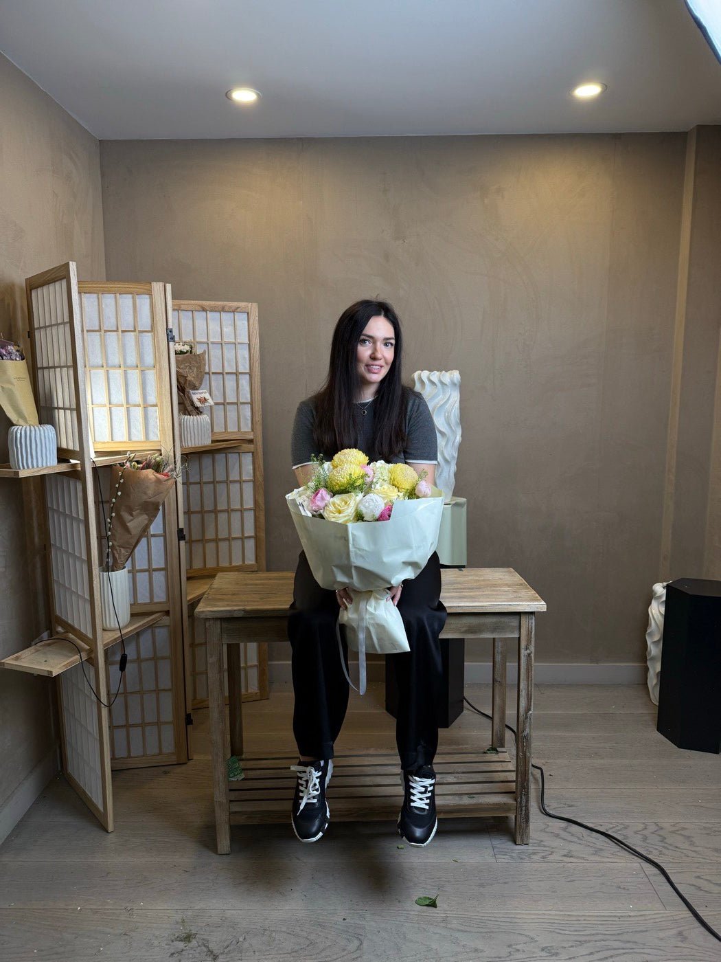 Olga Sheppard sitting on a work table in the Upper East Side studio holding a wrapped bouquet