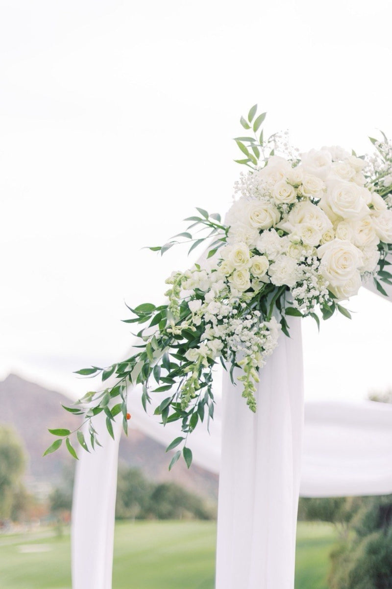 White rose and baby&rsquo;s breath arrangement on a draped ceremony arch