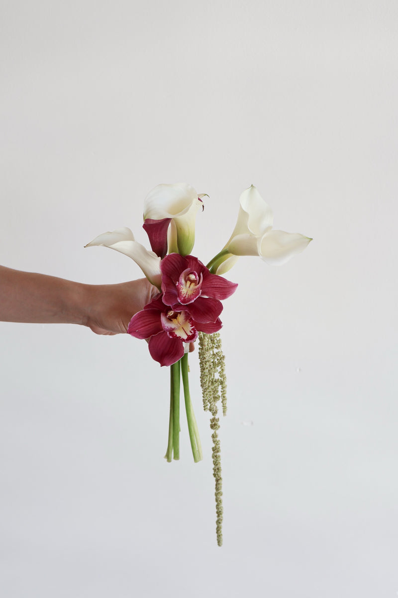 Small bouquet of white and burgundy calla lilies with cymbidium orchids and trailing green amaranthus