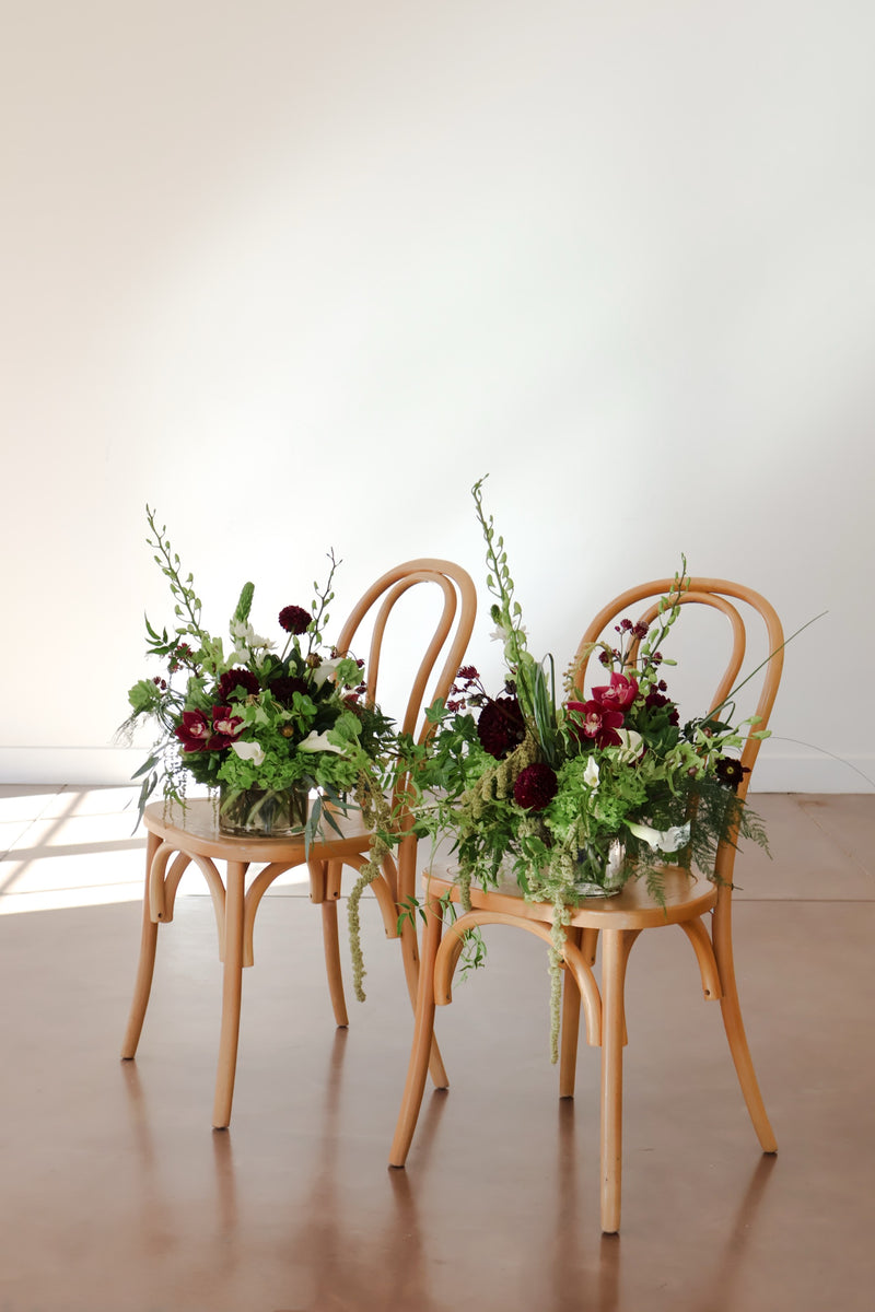 Pair of burgundy and green arrangements on bentwood chairs with green hydrangea calla lilies and cymbidium orchids