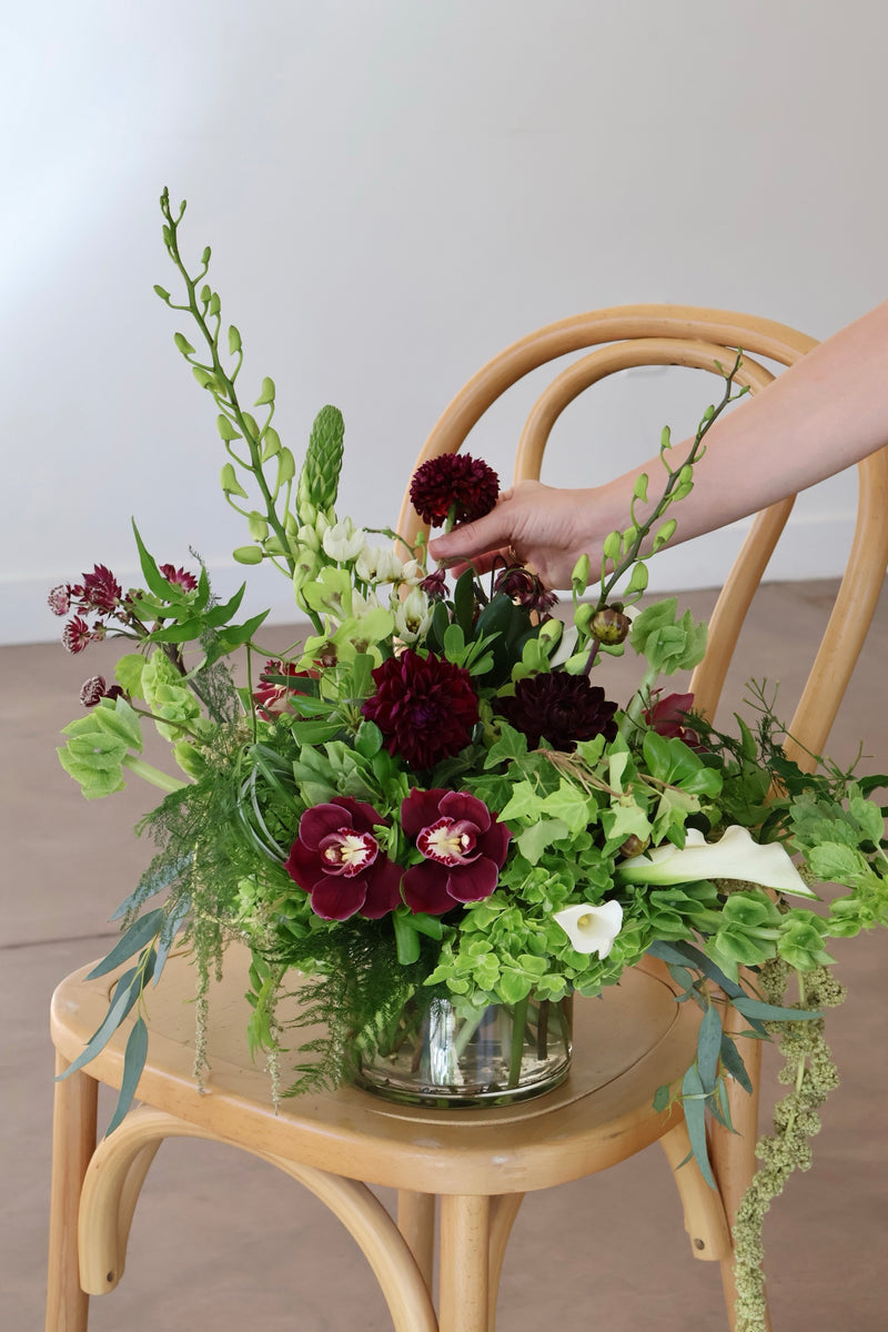 Florist placing a burgundy dahlia into a green hydrangea and ivy arrangement with white calla lilies
