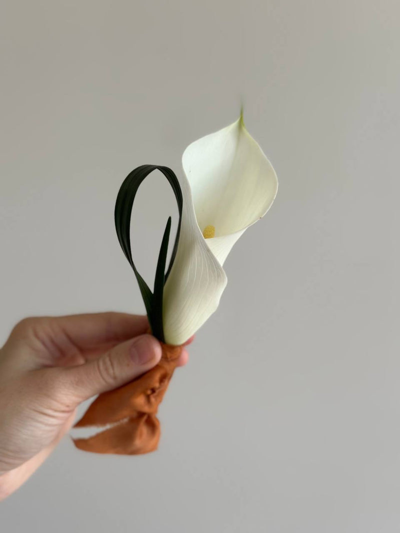Single white calla lily boutonni&egrave;re tied with a rust silk ribbon