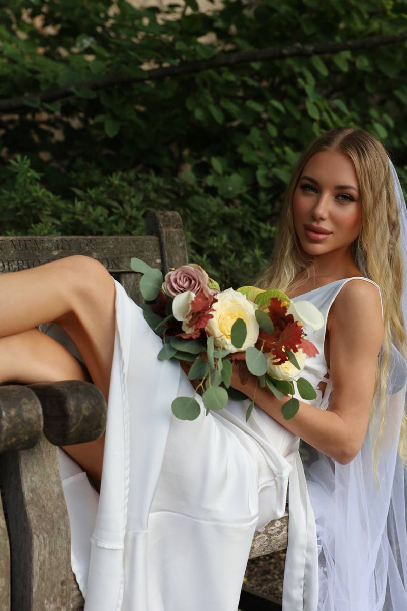 Bride seated on a park bench with a mauve cream and oak-leaf bouquet