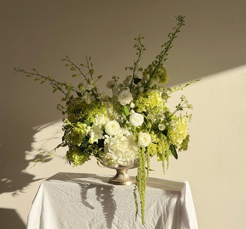 Green and white hydrangea rose and delphinium arrangement in a silver footed urn