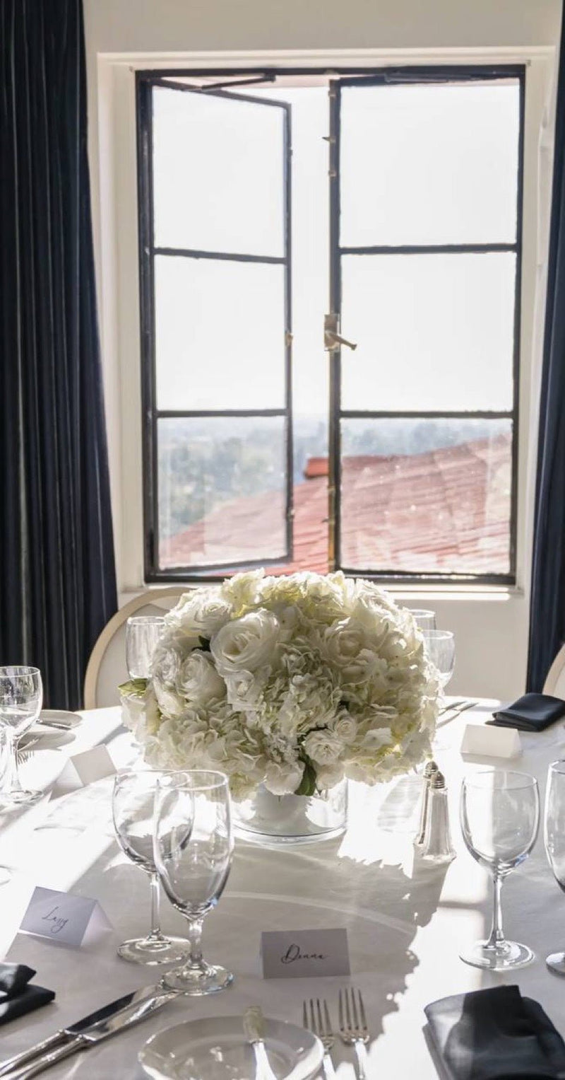 White rose and hydrangea centrepiece on a set table by an open window