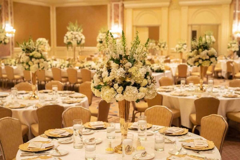 Ballroom of round tables with tall white and gold centrepieces