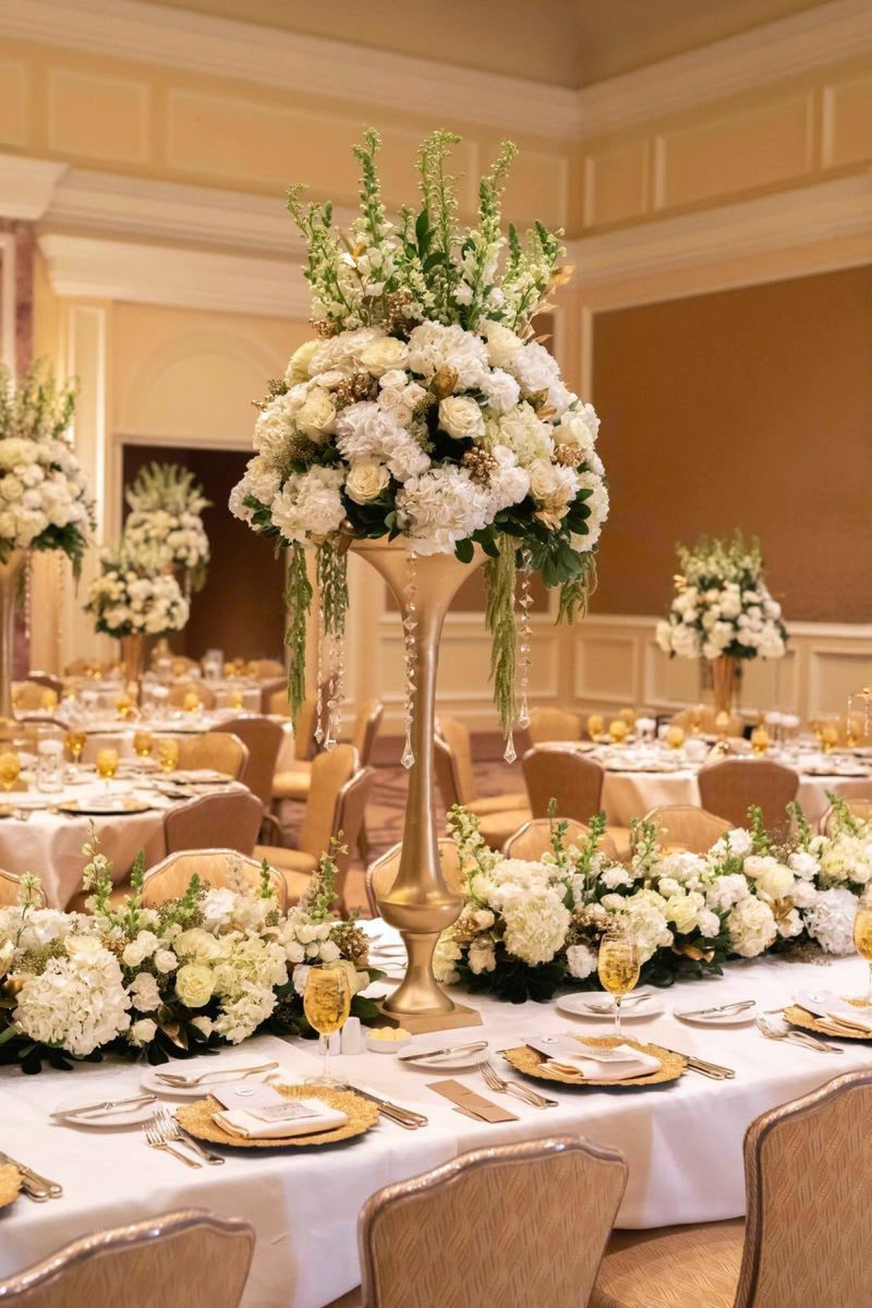 Tall gold pedestal centrepiece of white hydrangea roses and stock